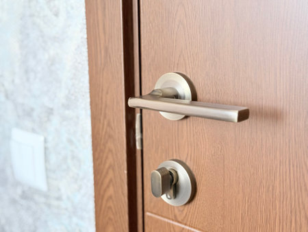 A close-up of a wooden door with a modern metal handle and thumb-turn lock.の写真素材