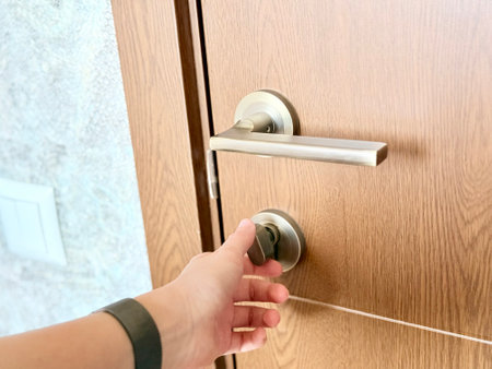 A close-up of a hand turning a modern metal thumb-turn lock on a wooden door with a sleek handle.の写真素材