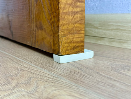 Improvised door stopper using a white rubber eraser under an old wooden door on a laminate floor.の写真素材
