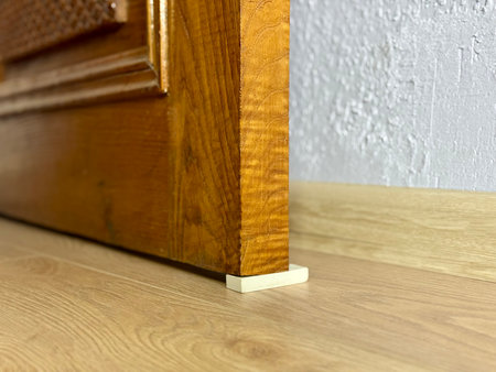 Improvised door stopper using a white rubber eraser under an old wooden door on a laminate floor.の写真素材