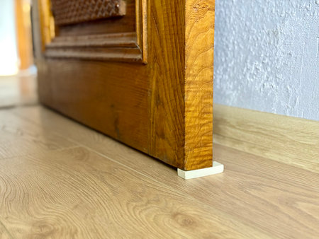 Improvised door stopper using a white rubber eraser under an old wooden door on a laminate floor.の写真素材