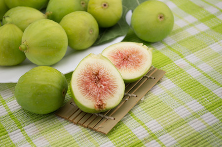 fig fruit on white background with green leaf and shove bamboo over a tablecloth with open fig and red pulp of a biological natureの写真素材