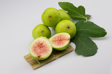 fig fruit on white background with green leaf and shove bamboo over a tablecloth with open fig and red pulp of a biological natureの写真素材