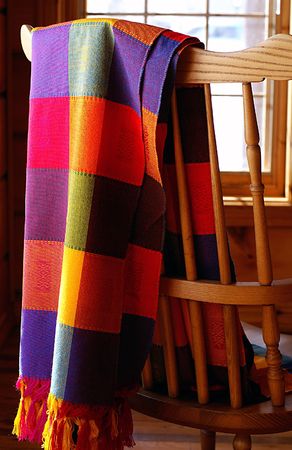 Vibrantly coloured Mexican cloth draped over a combback chair in log home.の写真素材