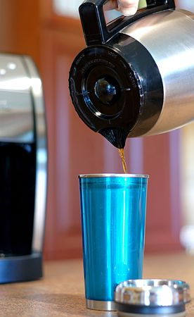 Pouring coffee into a travel mug from a carafe at homeの写真素材