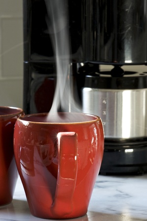 Steaming hot coffee in a red cup brewed at home saves money during an economic downturn.の写真素材
