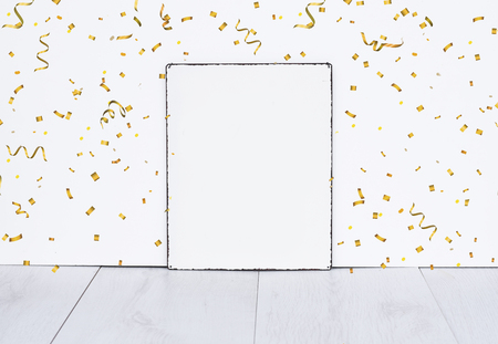 White empty board standing on grey wooden floor against white isolated wall with golden party confetti mock up for birthday or partyの写真素材