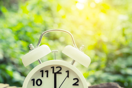 half of white alarm clock with blurred background and sun light vintage filter