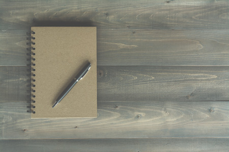 notebook and pen on wooden background with vintage filter