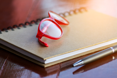 Red Glasses On Notebook with Pen and Wood Backgroundの写真素材