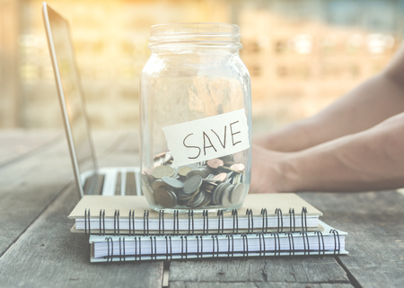 money for saving in glass jar on note book and laptop with vintage lightの写真素材
