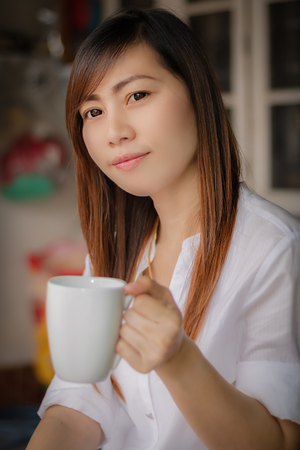 Portrait of young beautiful Asian woman holding white  cup of tea or coffee and happy  in the morning / selective focusの写真素材