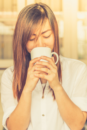Portrait of young beautiful Asian woman holding white  cup of tea or coffee and happy  in the morning / selective focusの写真素材