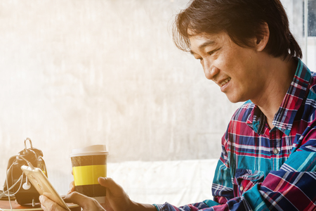 Male Asian touch smart phone and drinking coffee in a coffee shop.の写真素材