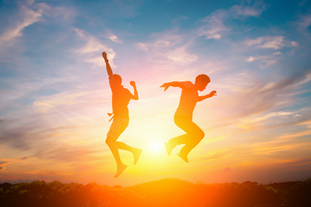 Silhouette of happy people jumping in sunset.の写真素材