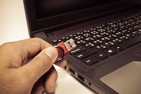 USB red flash drive stick being connected to notebook, selective focus