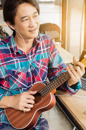 Asian man playing a ukulele in a coffee shop.の写真素材