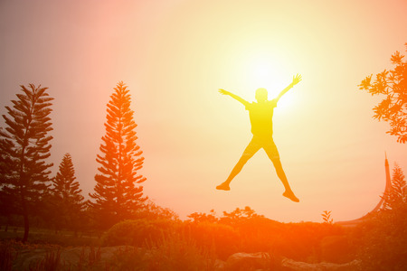 Silhouette of happy people jumping in sunset.の写真素材