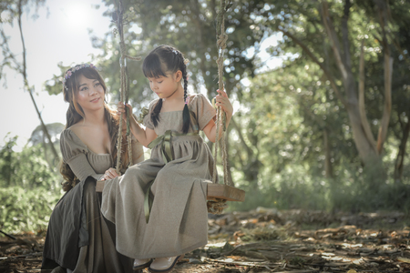 The sister is swinging to her sister under the shady trees in the tropical forest.の写真素材
