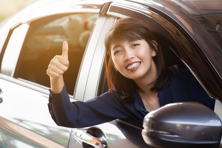 Happy Asian womanl in a car showing thumb up and smile in the morninggo to travel by a car.の写真素材