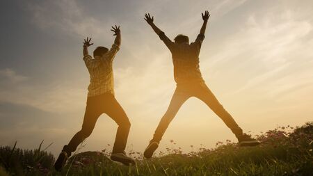 Silhouette of happy people jumping in sunset.の写真素材