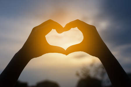 human hands in heart shape framing in sunset