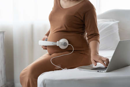 Beautiful Asian pregnant put headphone on her belly for baby songの写真素材