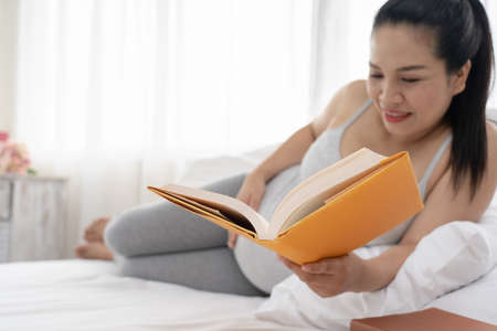 Happy Asian pregnant are reading a book in bedroom,pregancy conceptの写真素材