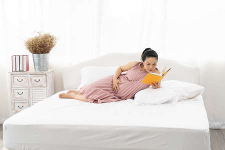 Happy Asian pregnant are reading a book in bedroom,pregancy conceptの写真素材