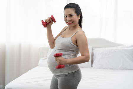 Pregnant women are exercising with dumbbells in the white bedroom.の写真素材