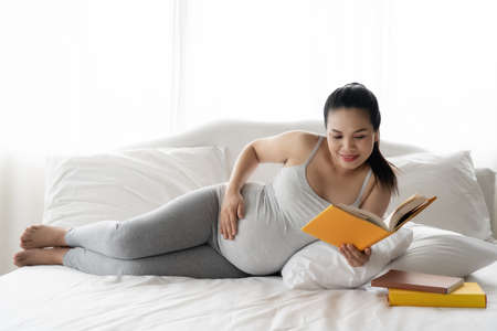 Happy Asian pregnant are reading a book in bedroomの写真素材