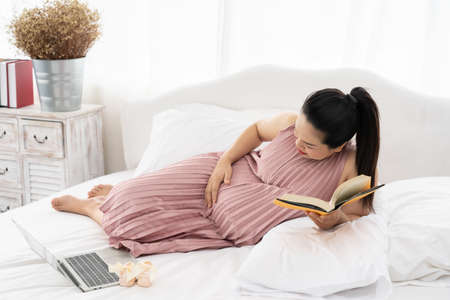 Happy Asian pregnant are reading a book in bedroom,pregancy conceptの写真素材