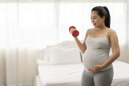 Pregnant women are exercising with dumbbells in the white bedroom.の写真素材