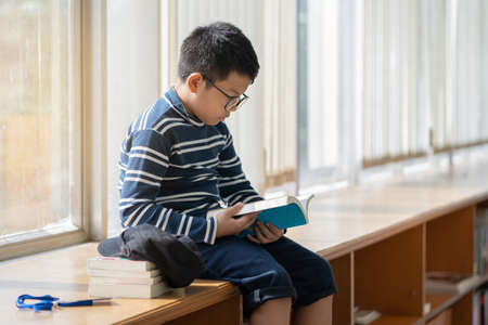 Asian boy reading a book in the library.