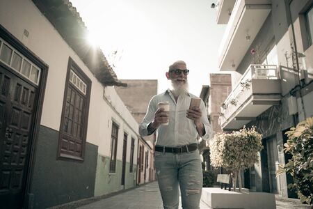 Trendy senior man using smartphone and drinking coffee. Mature male having fun with new technology trends - Beautiful lifestyle concept - Focus on this face - Imageの写真素材