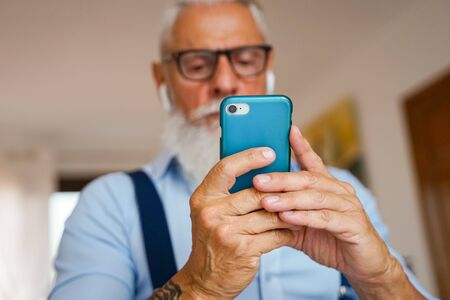 Attractive man in the house, changes songs and tracks on smartphone, listens to music in wireless headphones. Man with beard. focus hands - Imageの写真素材