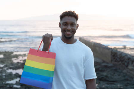 Young man hold a rainbow bag, gay boy. Concept of sexual minority and LGBT. Happy boy after of shopping near the beach. LGBT and holiday concept.の写真素材