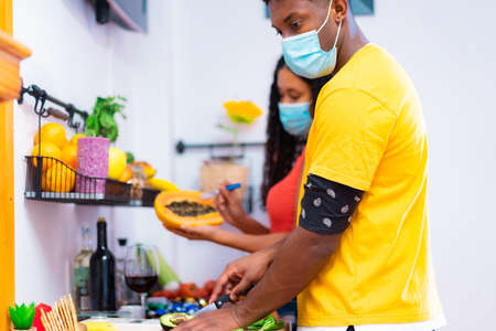 Young couple cooking in kitchen with protector masks for coronavirus. Friends while cooking healthy food in kitchen at home. Medical and food concept.の写真素材