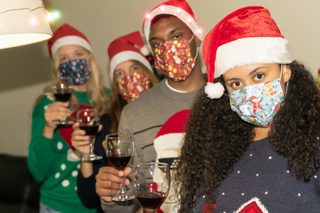 Friends drinking wine wearing protective face mask at the house for coronavirus in christmas time....