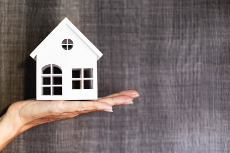 Hand holding a house model. Real estate agent offer house, property insurance and security. Buy and rent house concept. Gray background.の写真素材