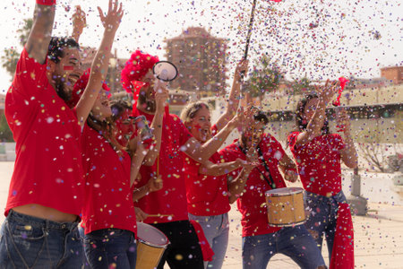 Football fan screaming, with red shirts out of the stadium throwing confetti. Group of young people very excited about football. Sport and fun concept.の写真素材