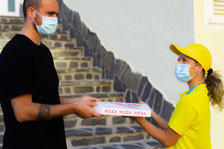 Delivery woman employee in yellow cap and t-shirt uniform face protective mask hold food order pizza box.の写真素材