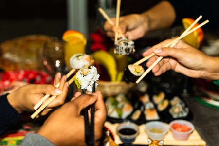 People hands hold sushi rolls with sticks. Couples eating and sharing sushi roll, maki, nigiri, uramaki. Food concept.の写真素材
