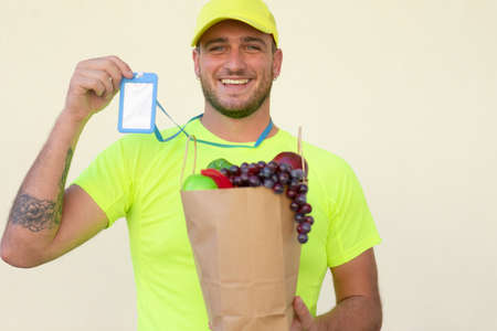 Caucasian delivery man worker in yellow color uniform handling bag of food, fruit and vegetable....