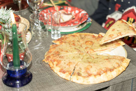 Person hand taking slice of pizza margherita. Big pizza margarita close up over christmas background.の写真素材