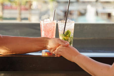 Male and female hands with cocktails. Closeup of couple hands, two cocktails. Romantic couple at drinking in a restaurant. Love, Marriage proposal and engagement concept.の写真素材
