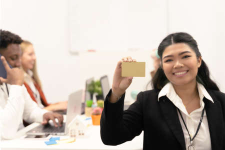 Happy smiling Asian business woman showing gold business card. Focus on gold card.の写真素材