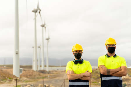 Front view of two skilled workers in a wind turbine power station. Two male electrician workers in reflective vests and hard hats. Clean energy, renewable energy and environment concept.の写真素材