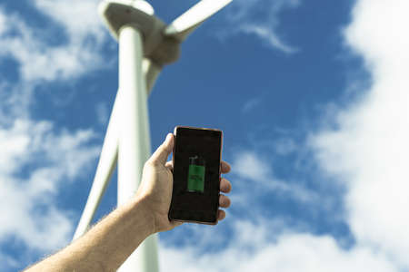 Hand portrait of caucasian man holding a smartphone, in the background a whirlwind. Renewable energy, future and electricity concept.の写真素材