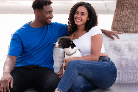 Young millennial couple with their dog. Young friends and dog sitting on a bench, waiting for other friends. Love, friendship and pet concept.の写真素材